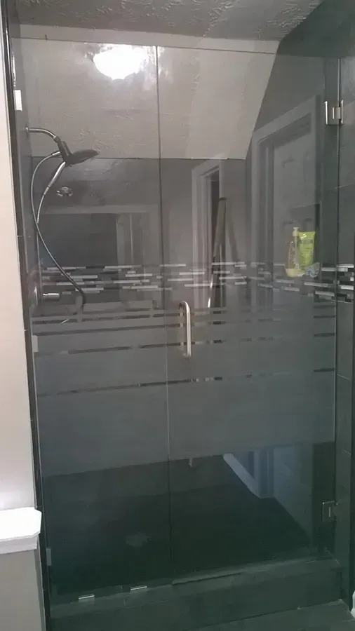Modern glass shower enclosure with chrome fixtures and frosted horizontal stripes.