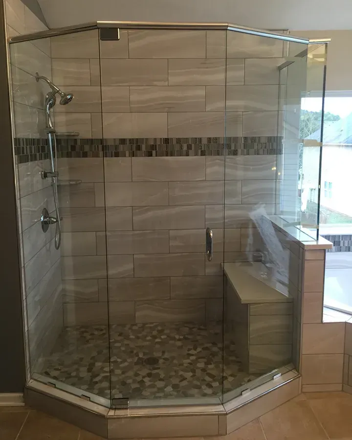 Glass walk-in shower with beige tile, pebble floor, and built-in bench