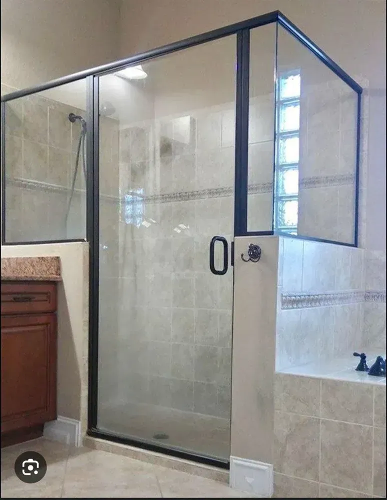 Frameless glass shower enclosure with dark trim in a tiled bathroom