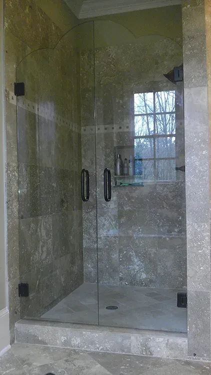 Glass shower enclosure with stone tile walls and a window reflection