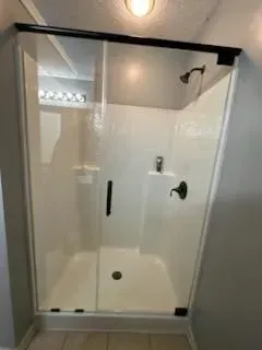 Walk-in shower with glass door, white tile walls, and black hardware