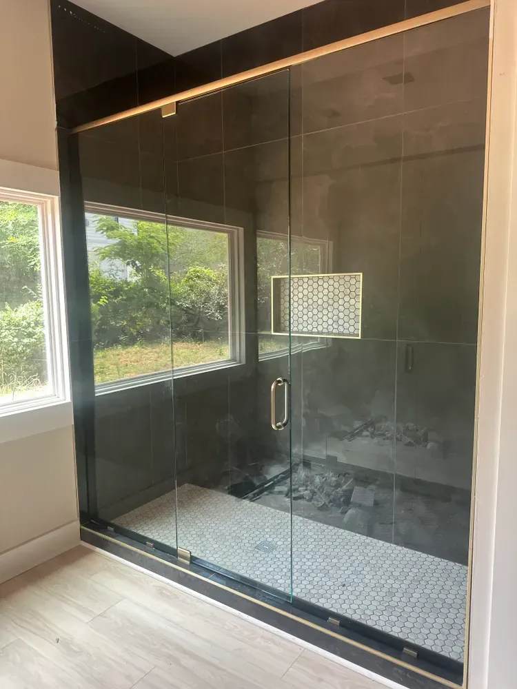 Modern glass walk-in shower with black tile, bench, and window views into greenery