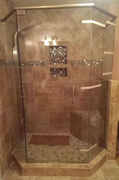 Glass-enclosed corner shower with beige tile walls and a built-in bench