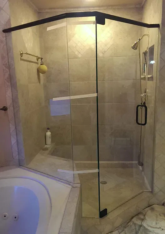 Corner glass shower enclosure in a beige tiled bathroom with a bathtub nearby