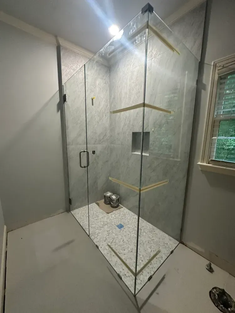 Glass-enclosed shower under construction in a bathroom, with tiled walls and floor.
