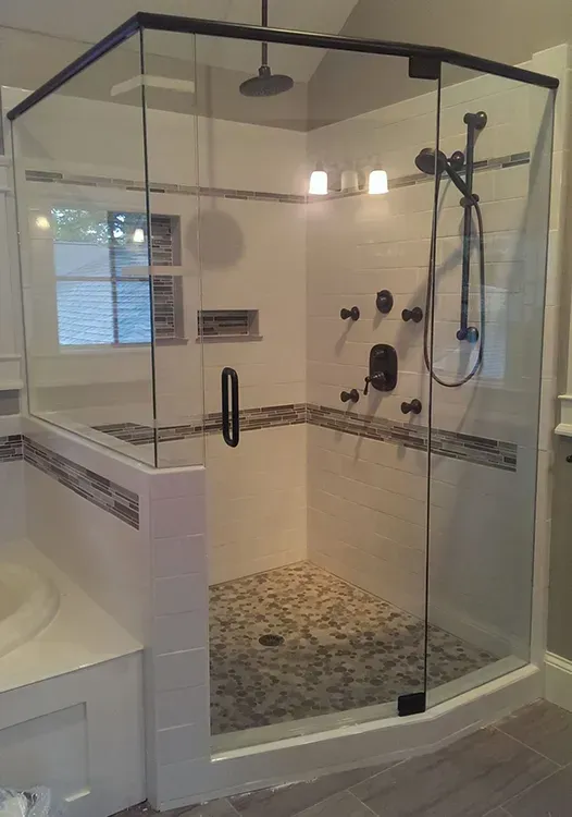 Glass walk-in shower with marble tile, built-in bench, and black fixtures in a bright bathroom