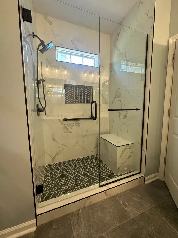 Modern glass shower with black hardware, mosaic tile floor, and built-in bench in a tiled bathroom.