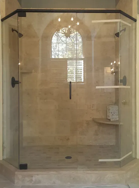 Glass shower enclosure with beige tile, built-in shelf, and arched window reflected in the back wall