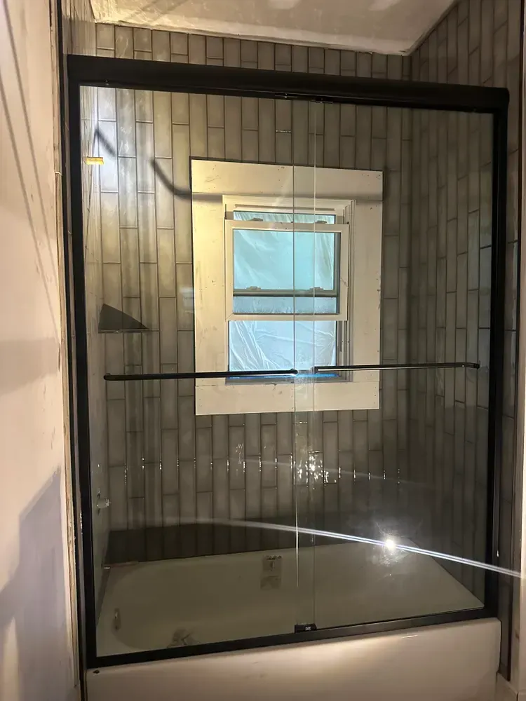Black-framed glass shower enclosure with tiled walls and a window inside.