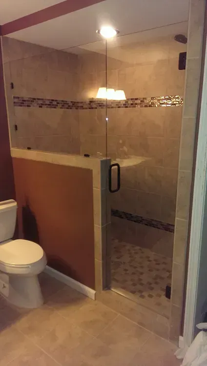 Glass shower enclosure beside a toilet in a beige-tiled bathroom
