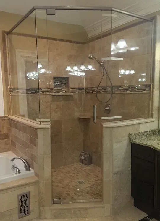 Glass-enclosed beige tiled shower with bench, handheld showerhead, and bronze fixtures in a bathroom