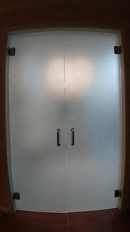 White double-door closet with black handles and corner bumpers against a wall.