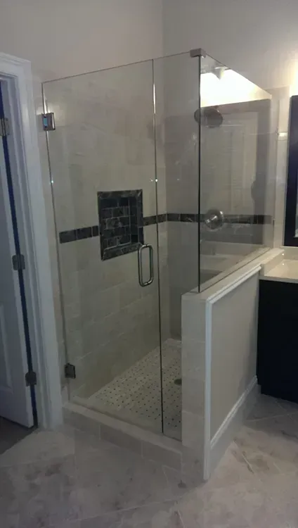 Glass walk-in shower with black tile accent and white half-wall in a bathroom