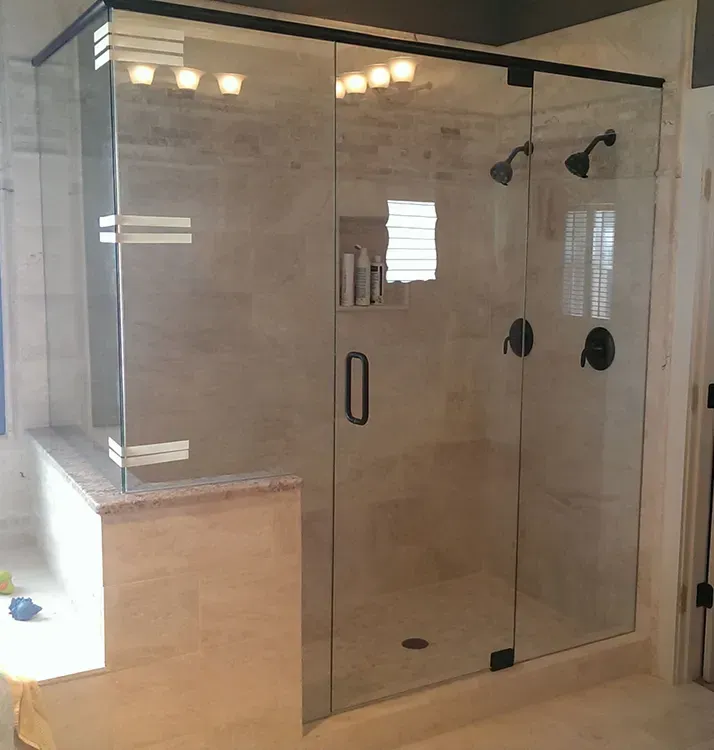 Glass shower enclosure in a light-tiled bathroom with built-in bench and black hardware
