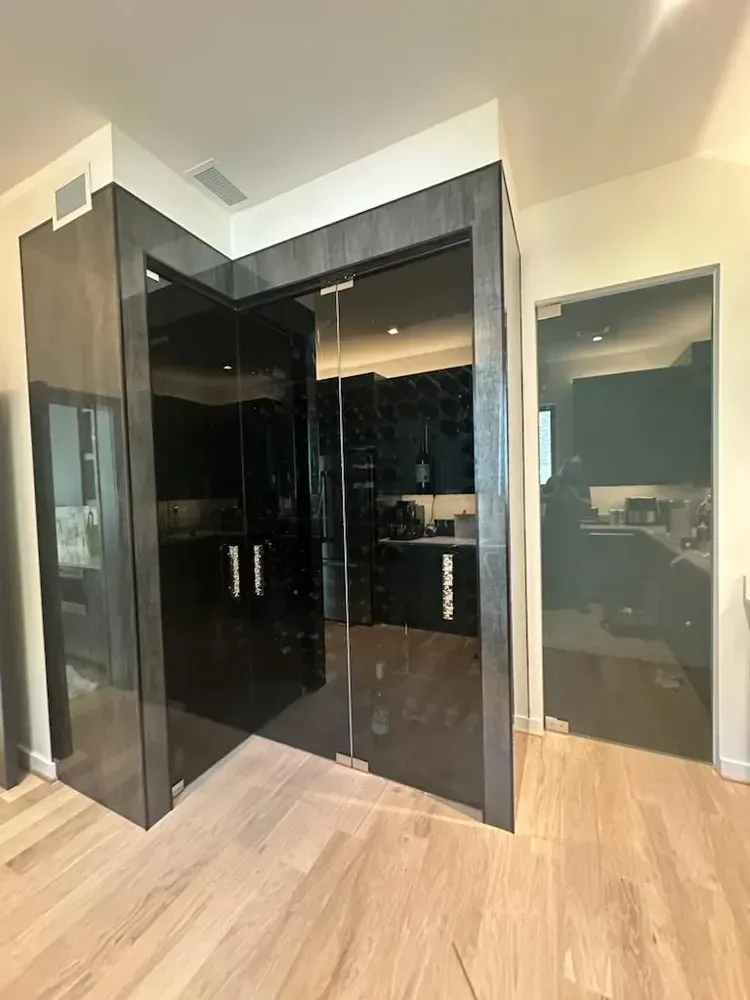 Modern kitchen with glossy black cabinets, glass doors, and light wood flooring