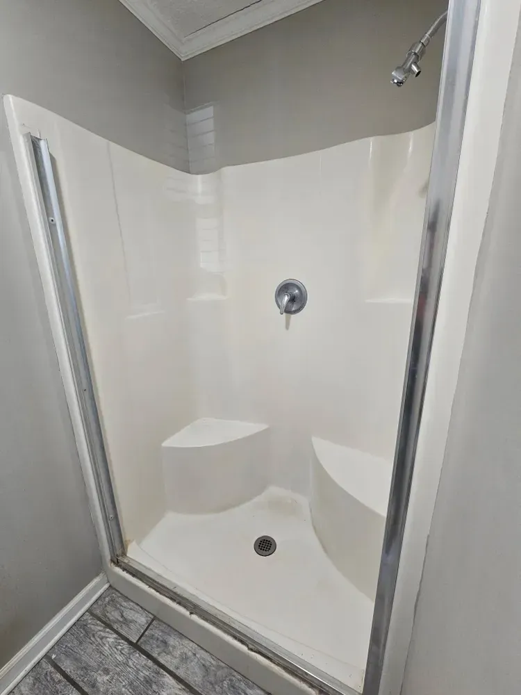 Empty white shower stall with built-in corner seat and chrome fixtures