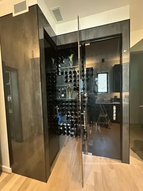 Modern wine cellar with glass door, black racks, and wood flooring in a contemporary home
