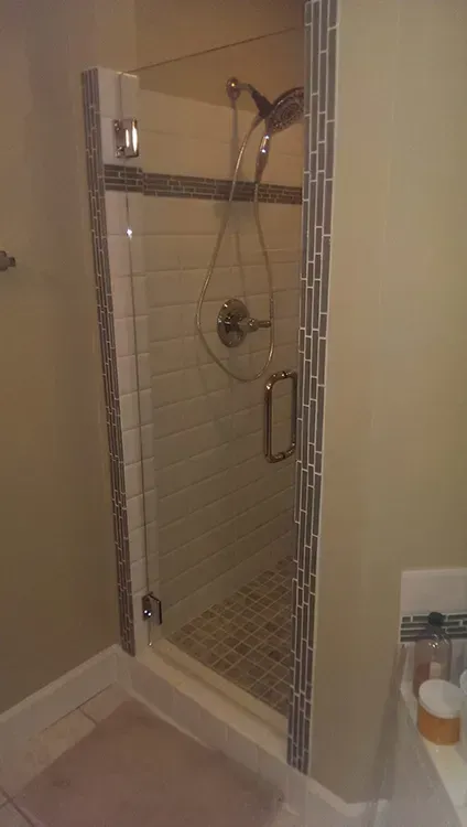Glass walk-in shower with chrome fixtures and beige tile walls in a bathroom.