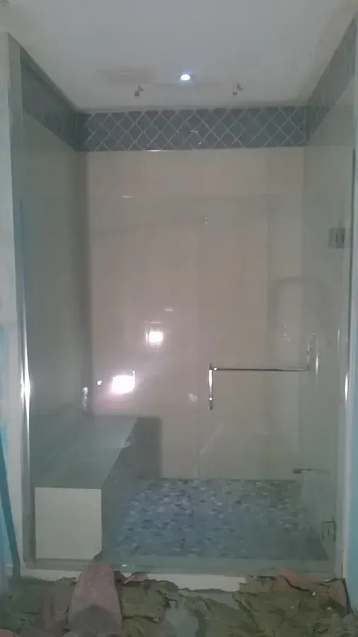 Empty tiled bathroom shower with a glass door and blue accent tile near the ceiling