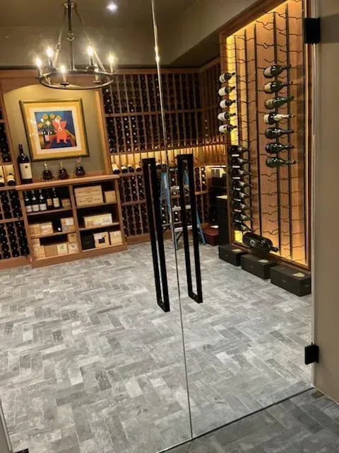 Wine cellar with glass doors, stone floor, wooden racks, and framed art in warm lighting