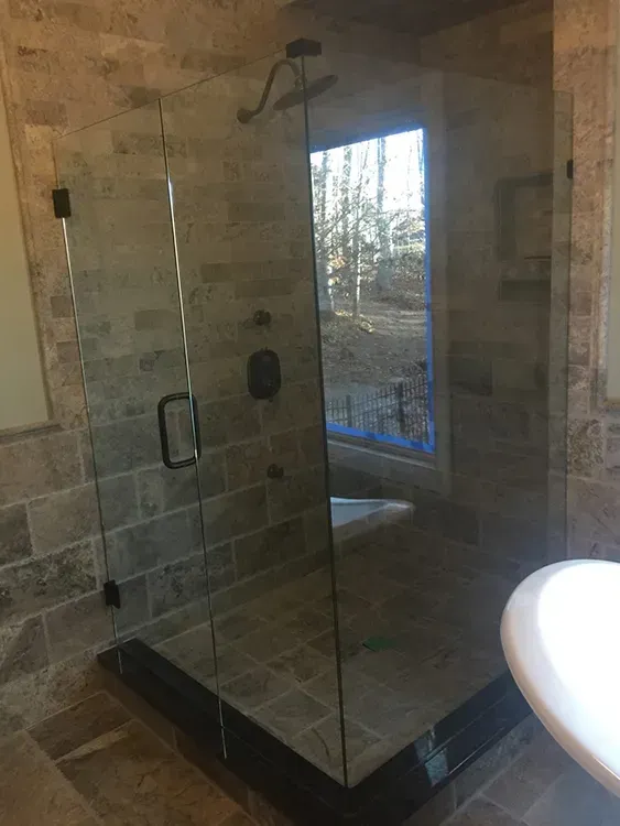 Glass walk-in shower with black base and stone tile walls in a bathroom