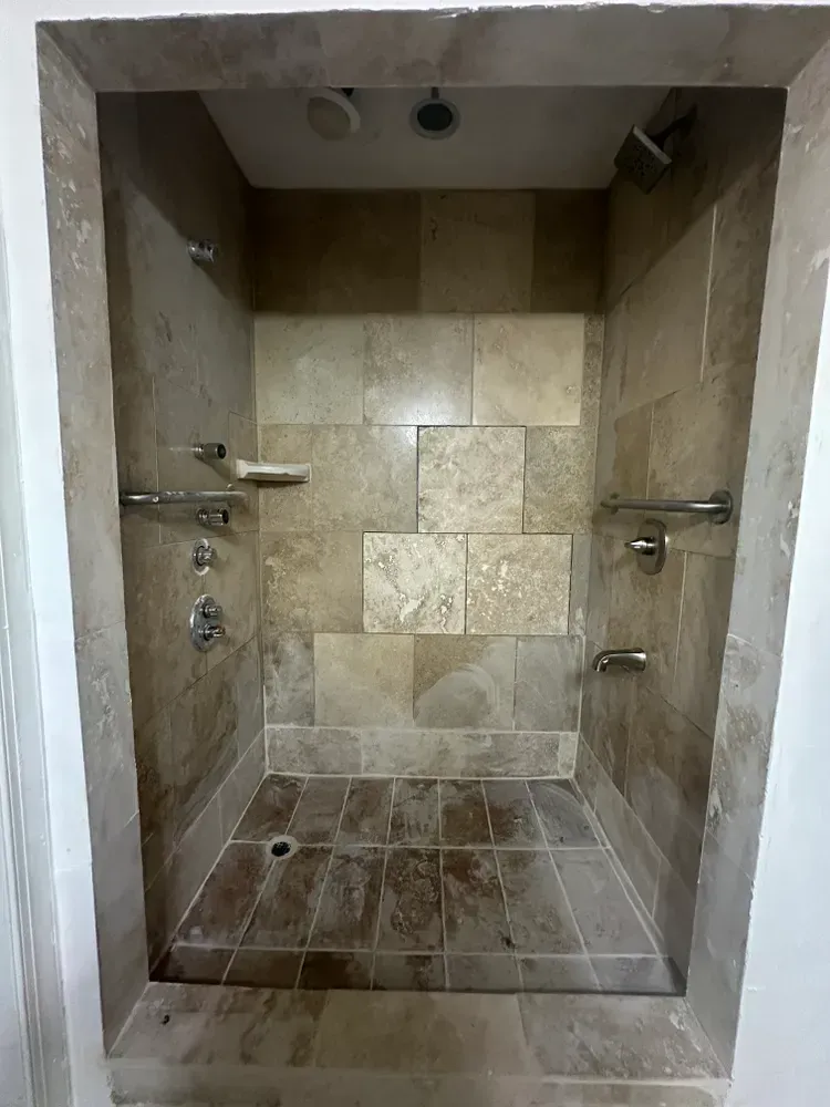 Empty tiled walk-in shower with beige walls, metal grab bars, and built-in shelves.