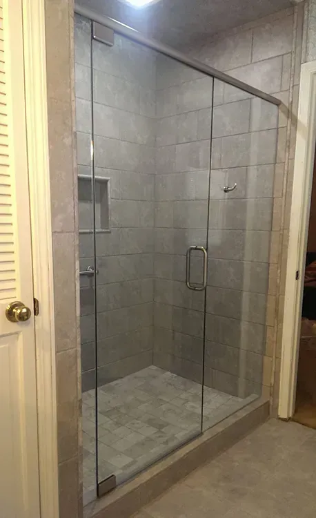 Glass shower enclosure in a tiled bathroom with a beige floor and chrome handle