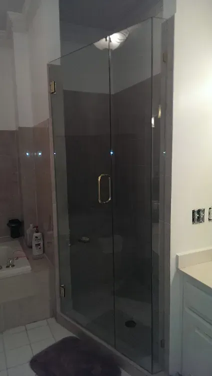 Dark glass shower enclosure in a bathroom with tiled walls and a showerhead above.
