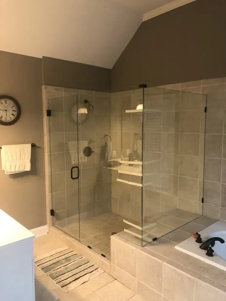 Modern beige bathroom with glass shower enclosure, freestanding tub, wall clock, and towel rack.