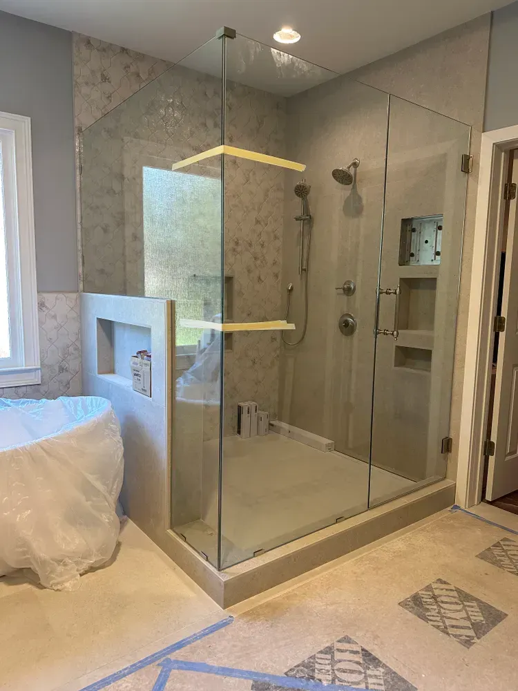 Glass walk-in shower with beige tile and gold trim in a modern bathroom