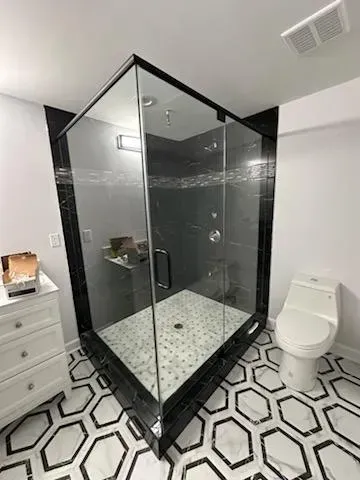 Modern bathroom with black-framed glass shower, hex tile floor, white toilet, and vanity drawers