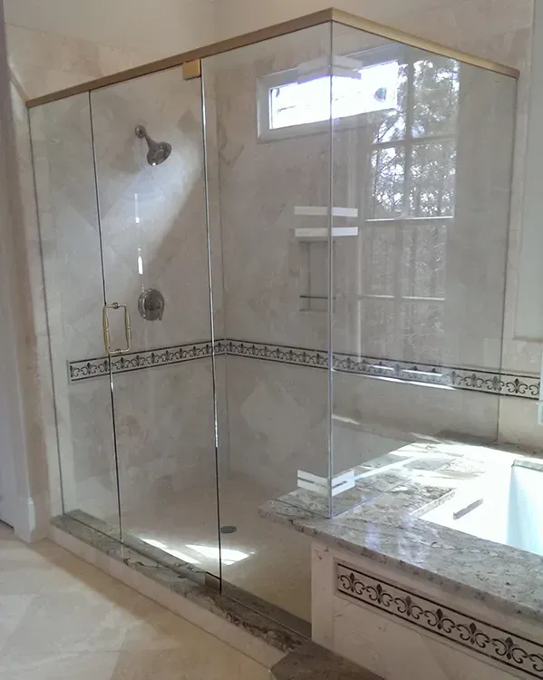 Glass-enclosed shower with beige tile, decorative border, and a bathtub edge on the right.