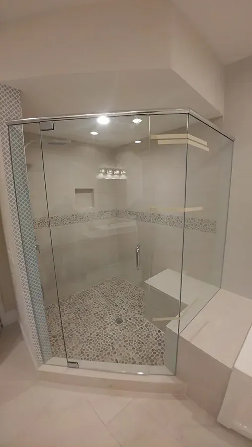 Glass shower enclosure in a tiled bathroom with a pebble-stone floor and wall-mounted shelf.