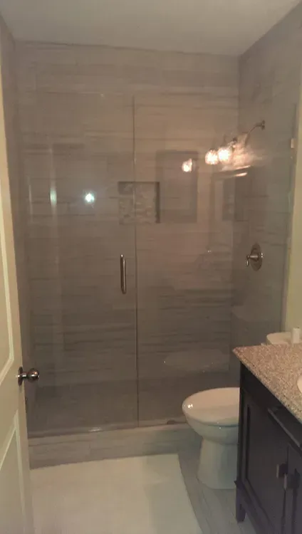 Small bathroom with a glass-enclosed shower, toilet, and granite vanity countertop.