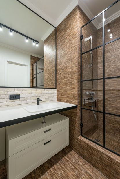 Modern bathroom vanity with white sink, mirror, brick tile walls, and glass shower enclosure