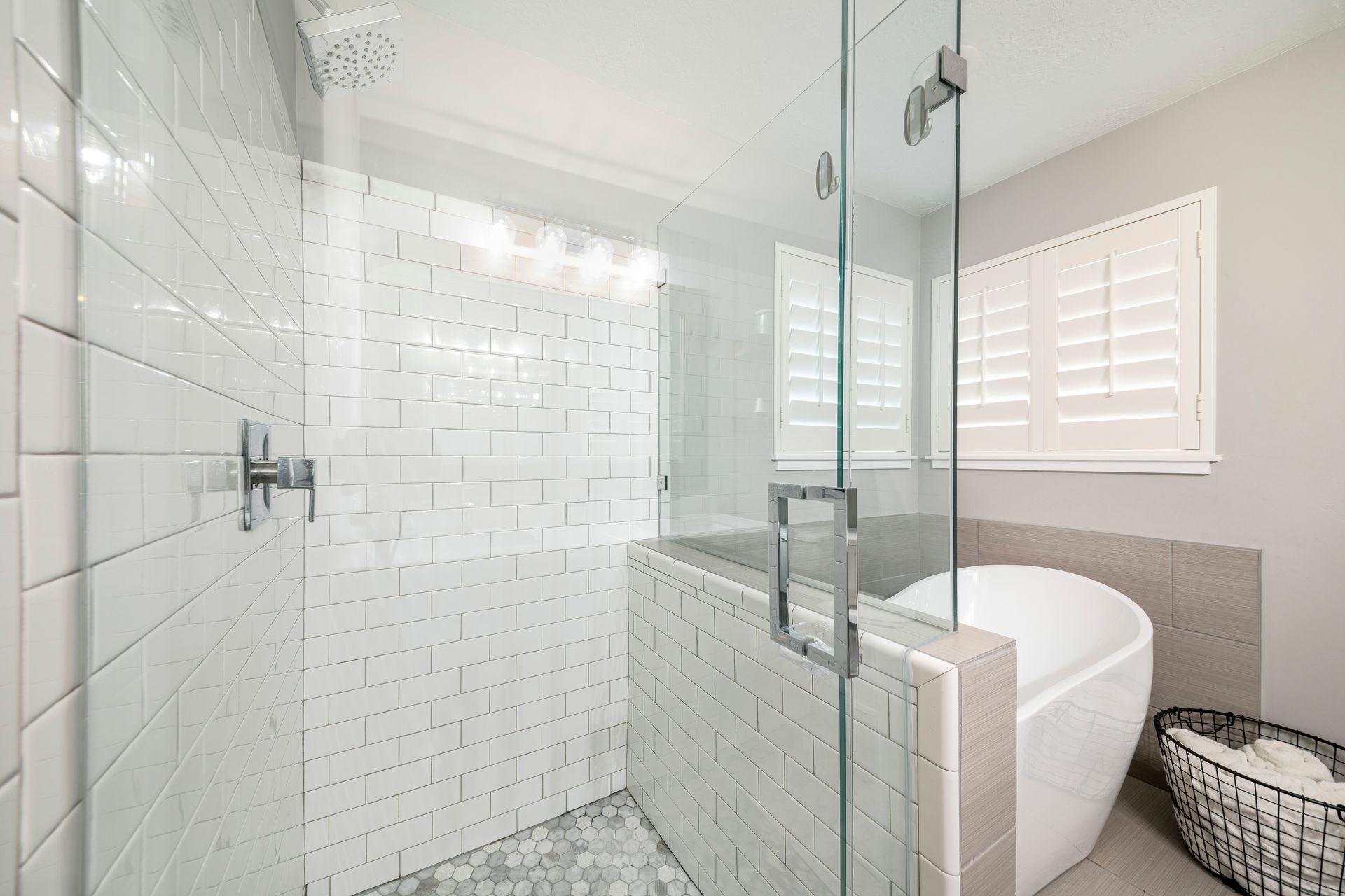Bright modern bathroom with glass shower enclosure, white tiled walls, and a freestanding tub by a window.