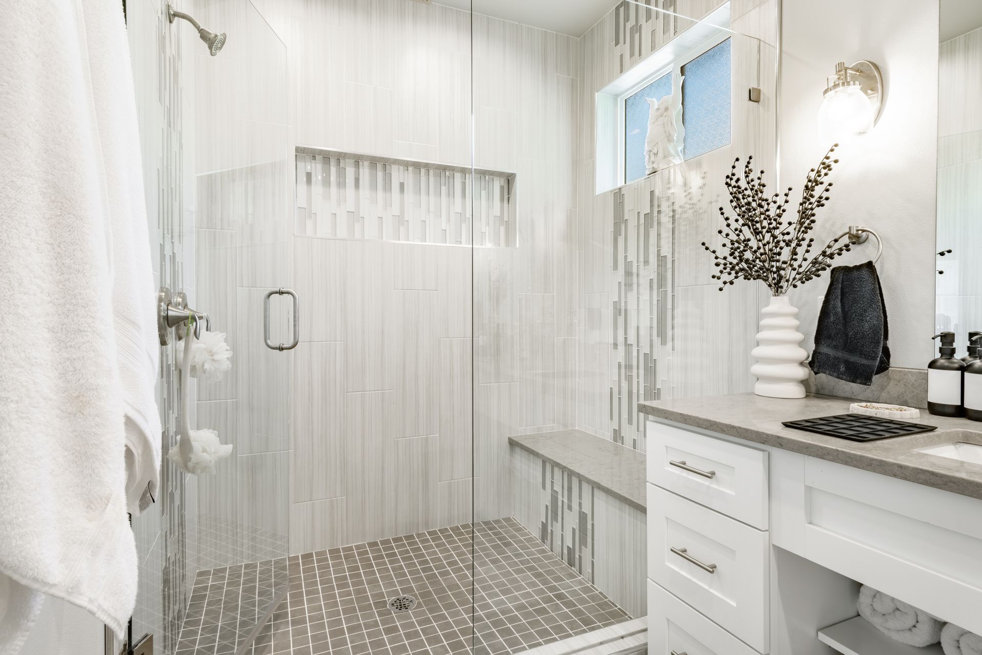 White tiled bathroom with walk-in shower, vanity, window, and black granite countertop