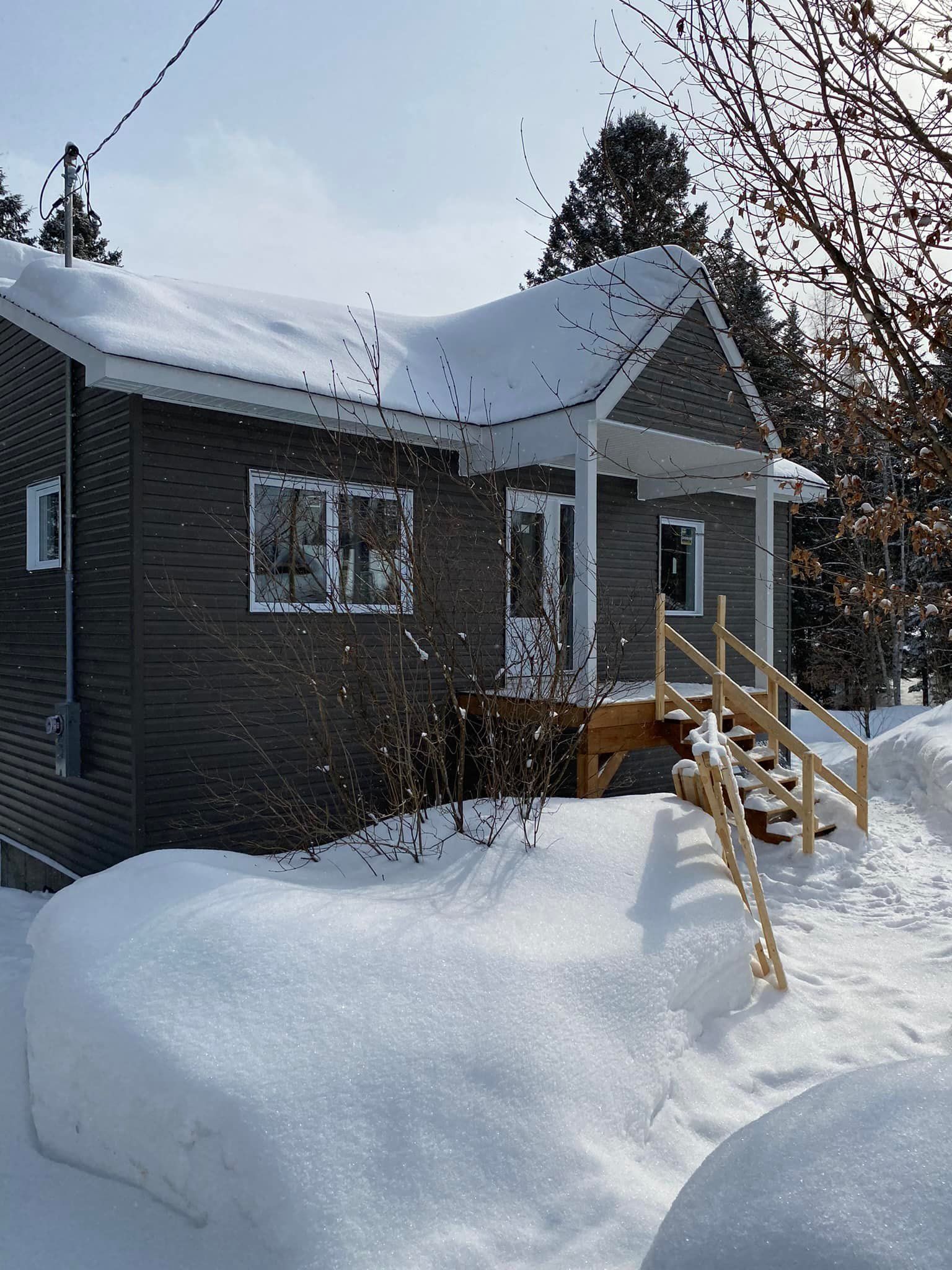 Une petite maison recouverte de neige, avec un porche et des marches en bois menant à la porte d'entrée.