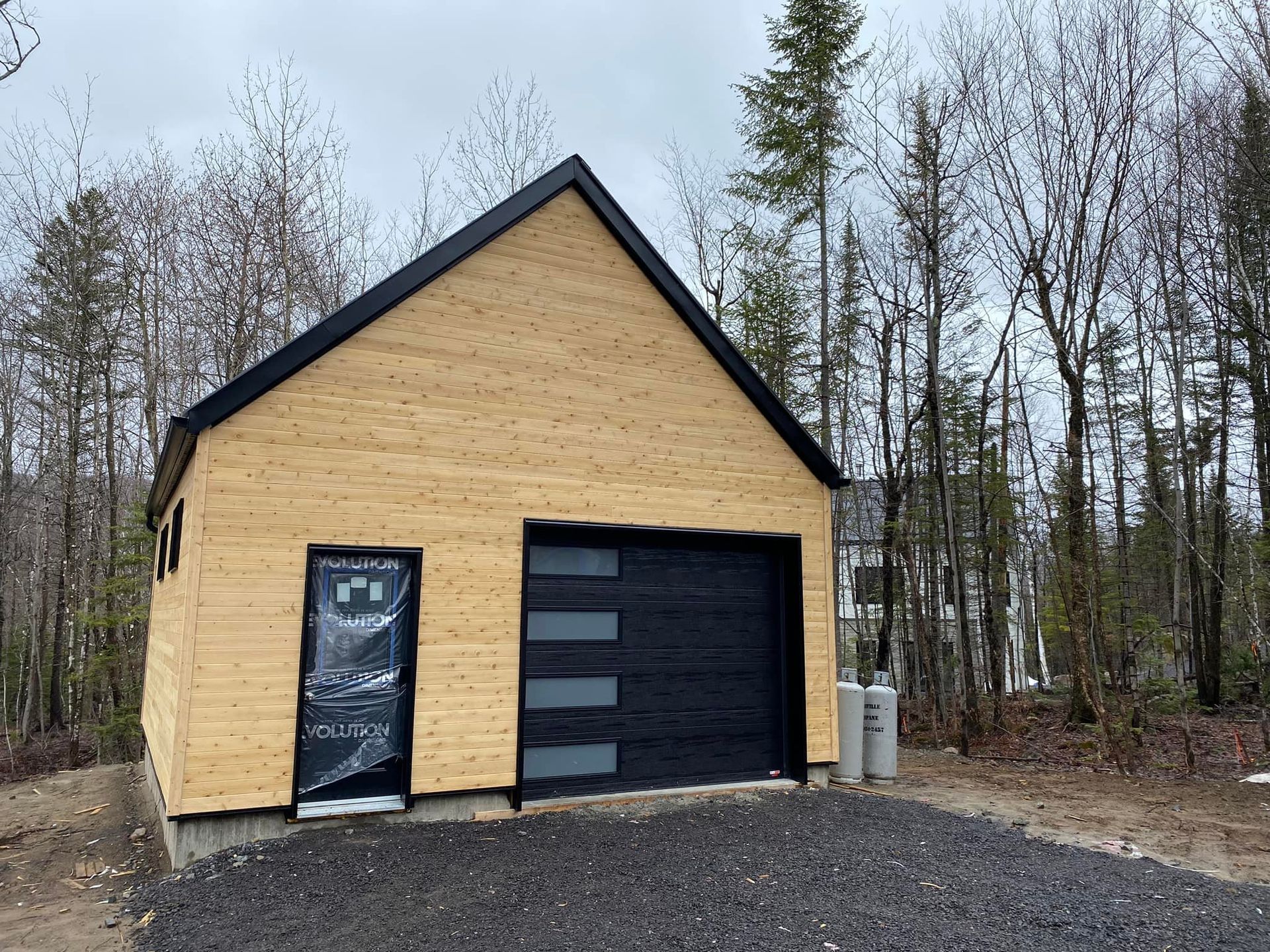 Structure en A avec porte de garage et porte noires, construite sur du gravier. Le toit est noir.