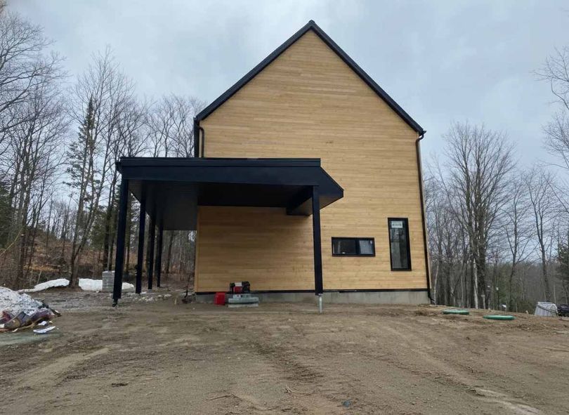 Maison moderne en bois avec abri voiture noir. Vue extérieure par temps nuageux.