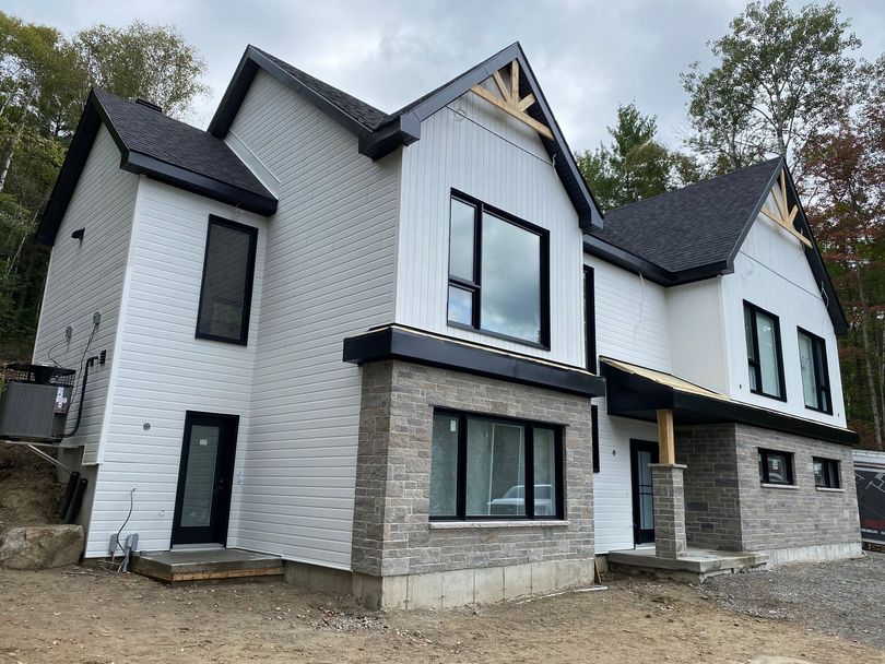 Maison moderne à deux étages avec toit noir, bardage blanc et éléments en pierre.