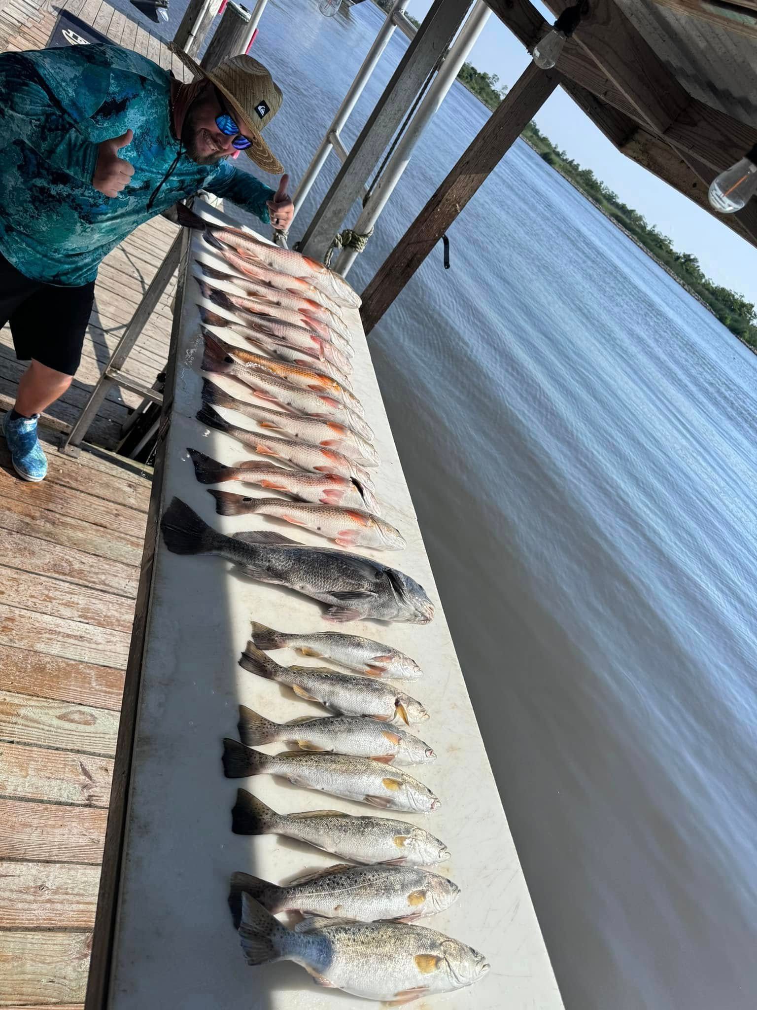 A man is standing next to a table full of fish on a dock.