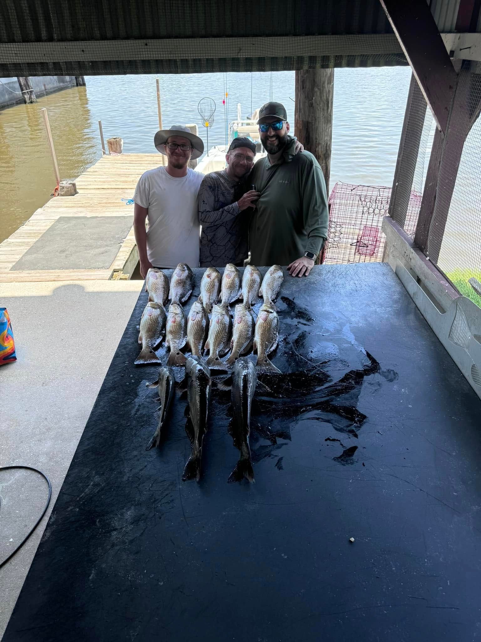 Three men are standing next to a table filled with fish.