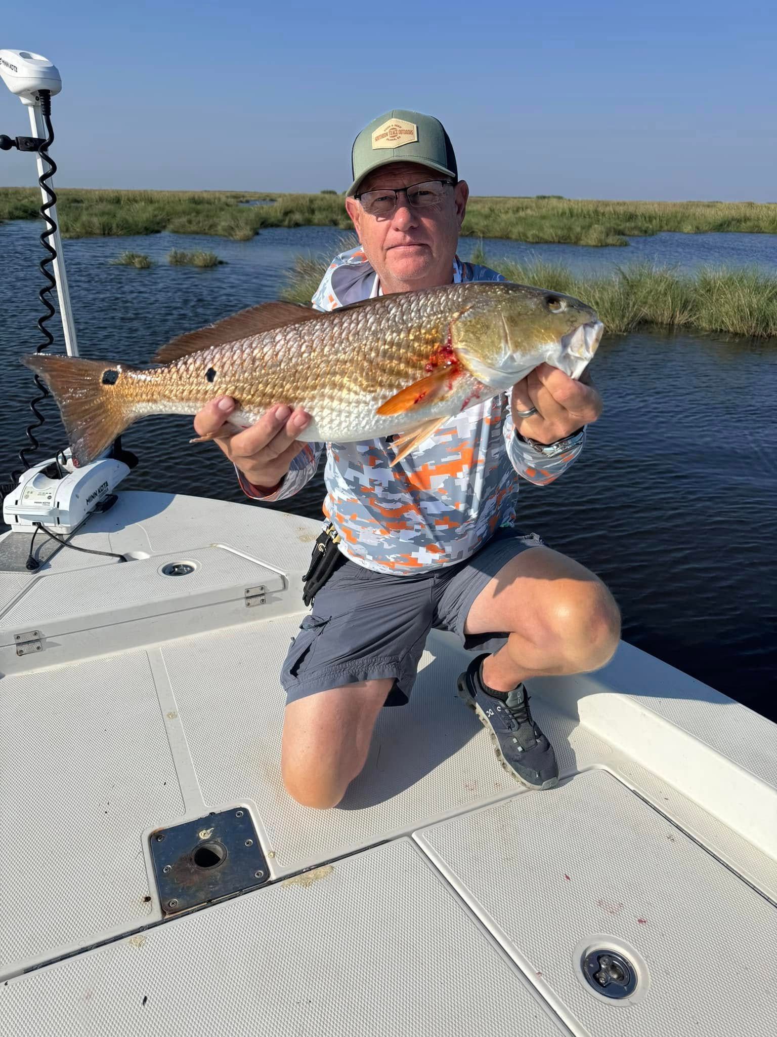 A man is kneeling on a boat holding a large fish.