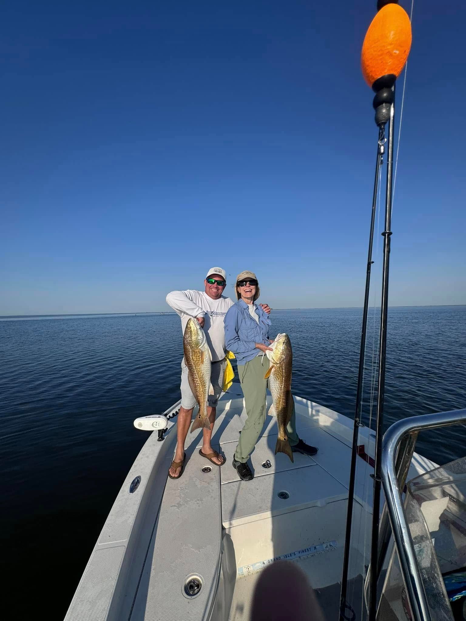 Two people are standing on the back of a boat holding fish.