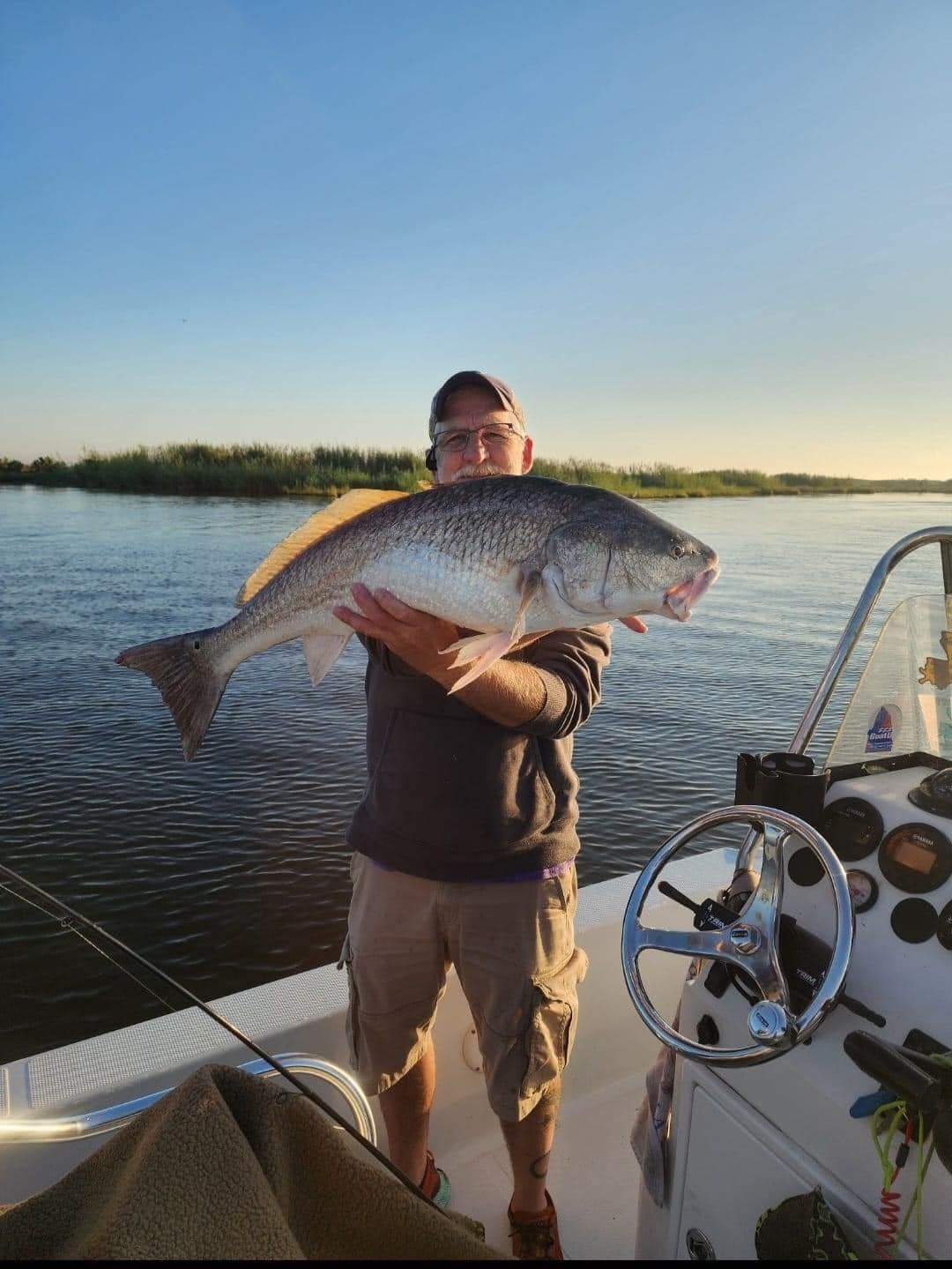 A man is standing on a boat holding a large fish.