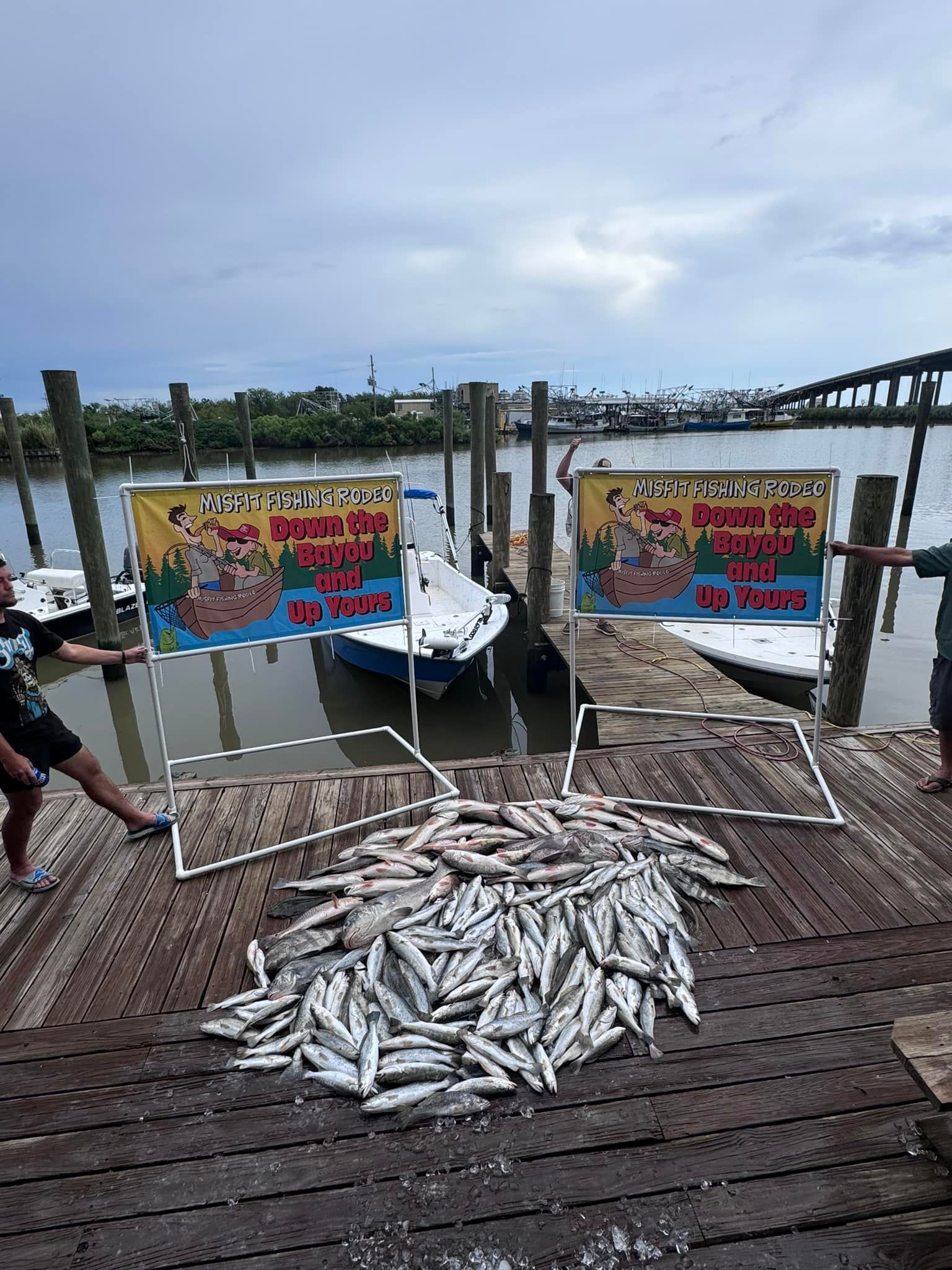 A pile of fish is sitting on a wooden dock next to a boat.