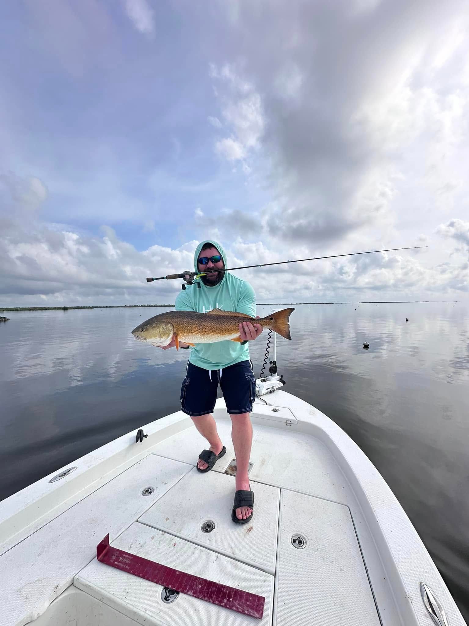 A man is standing on the back of a boat holding a large fish.