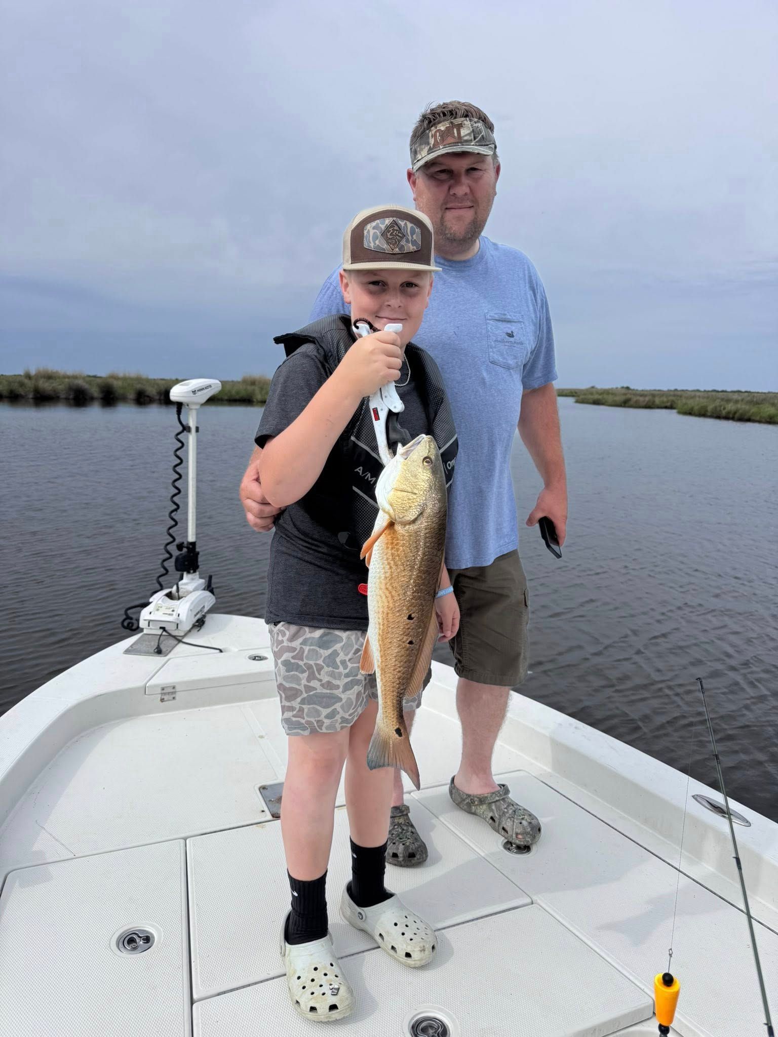 A man and a boy are standing on a boat holding a fish.