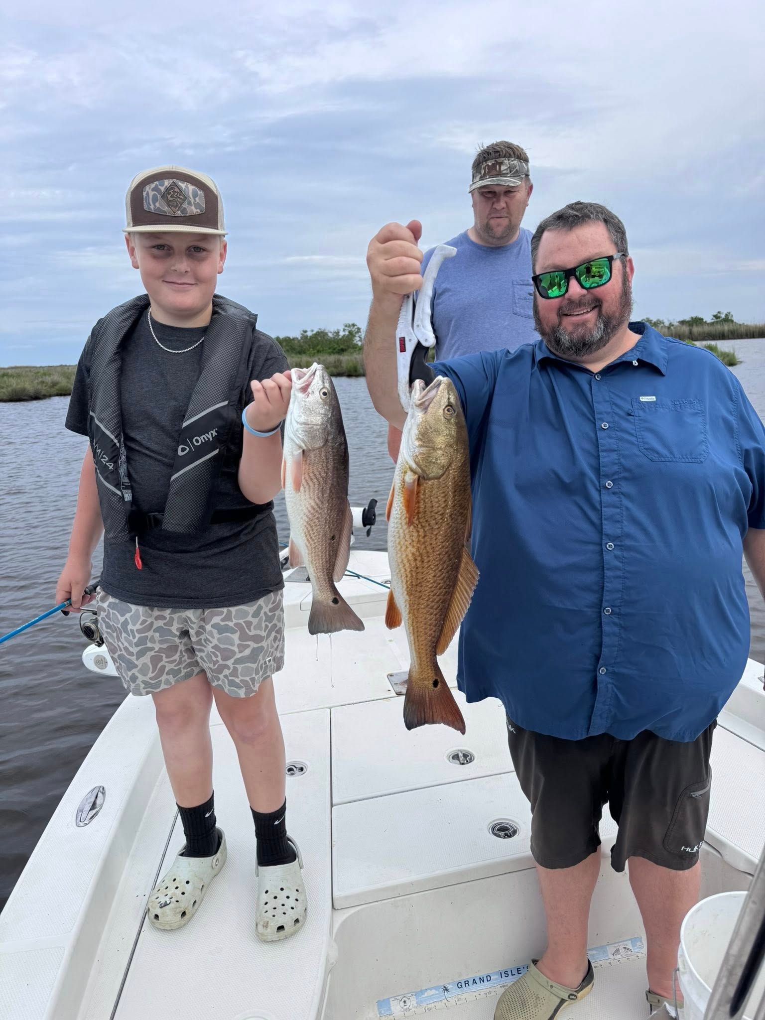 A man and two children are standing on a boat holding fish.